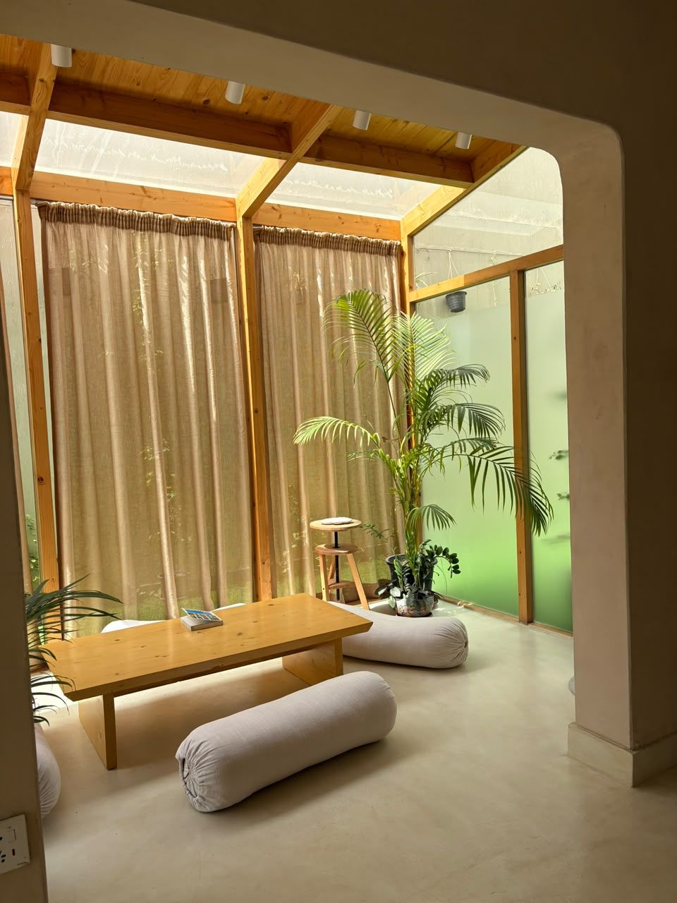The sunlit courtyard lounge with a low wooden table, floor bolsters and a tall palm