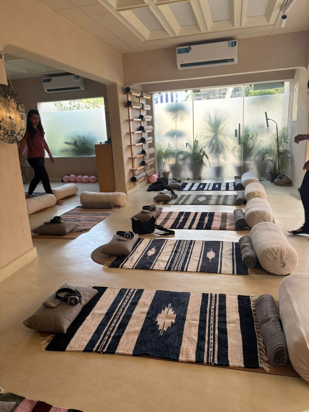 The DHA studio set up for class, with woven rugs, bolsters and frosted windows full of plants